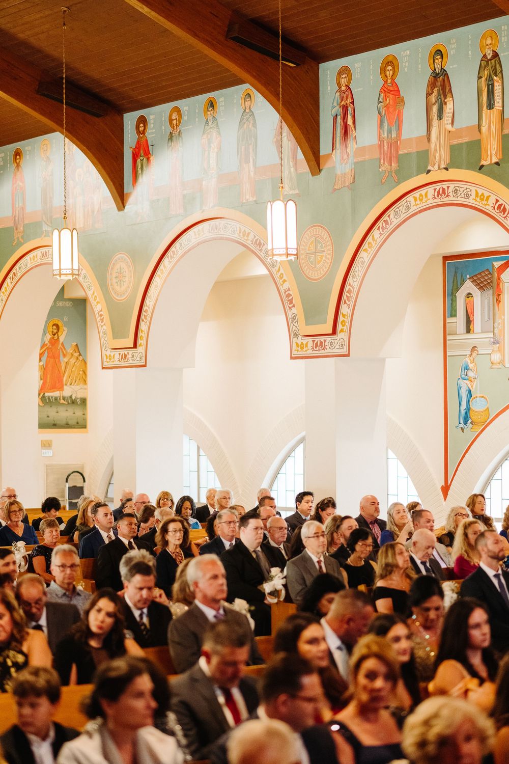 Elegant wedding ceremony in an Orthodox church with ornate religious artwork and icons decorating the walls.