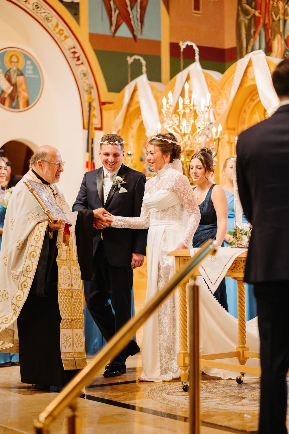Orthodox wedding ceremony taking place in ornate church with priests in white robes leading ritual celebrations.