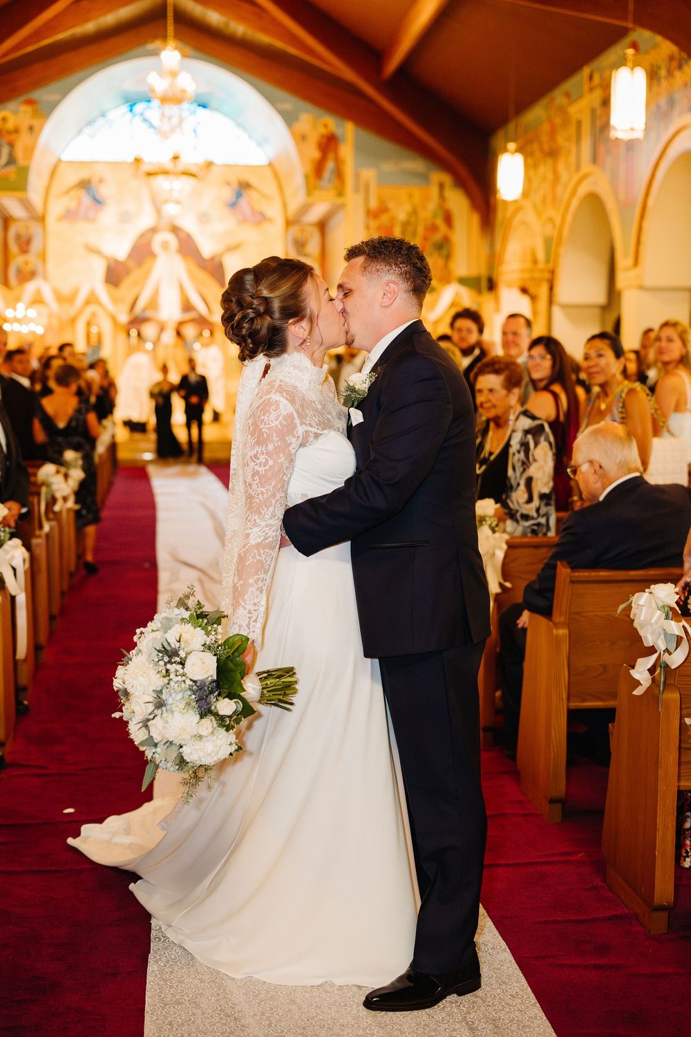 Elegant wedding ceremony inside an ornate church with warm lighting and red carpeted aisle.