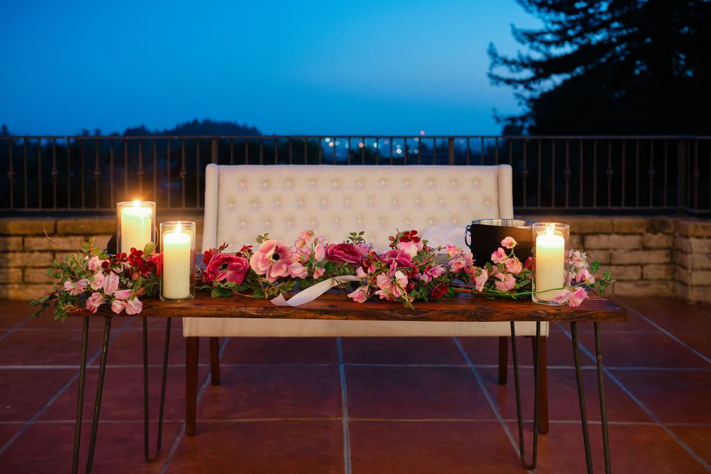 A memorial vigil display at dusk with flowers and candles arranged along an illuminated stone wall.