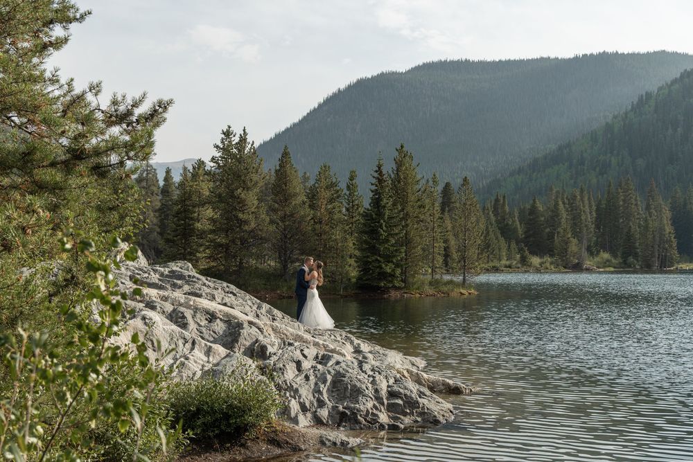 A scenic mountain lake shore panorama with evergreen trees and rocky outcrops along the tranquil water's edge.
