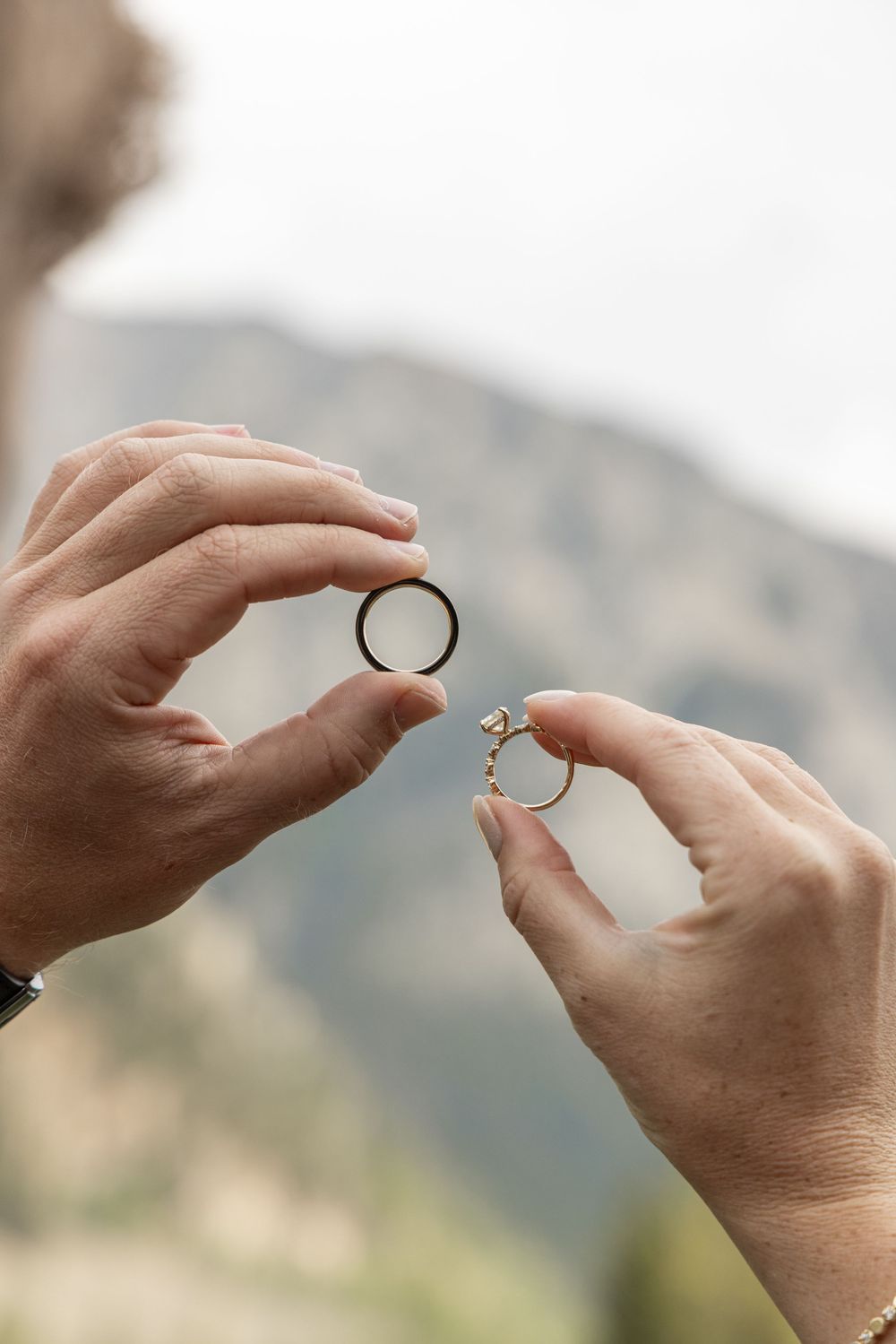 Four sequential images showing hands presenting and exchanging an engagement ring outdoors against a mountain backdrop.