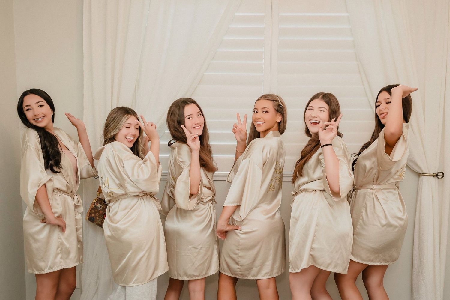 Wedding party wearing matching silk robes poses together in a bright indoor setting.