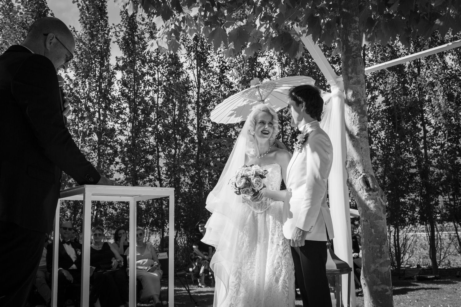 A black and white outdoor wedding ceremony under a canopy with a couple sharing an intimate moment.