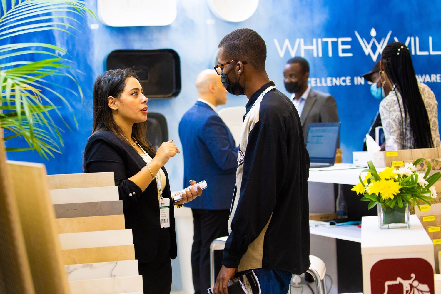 Business professionals networking and socializing at a corporate event with blue wall branding in the background.