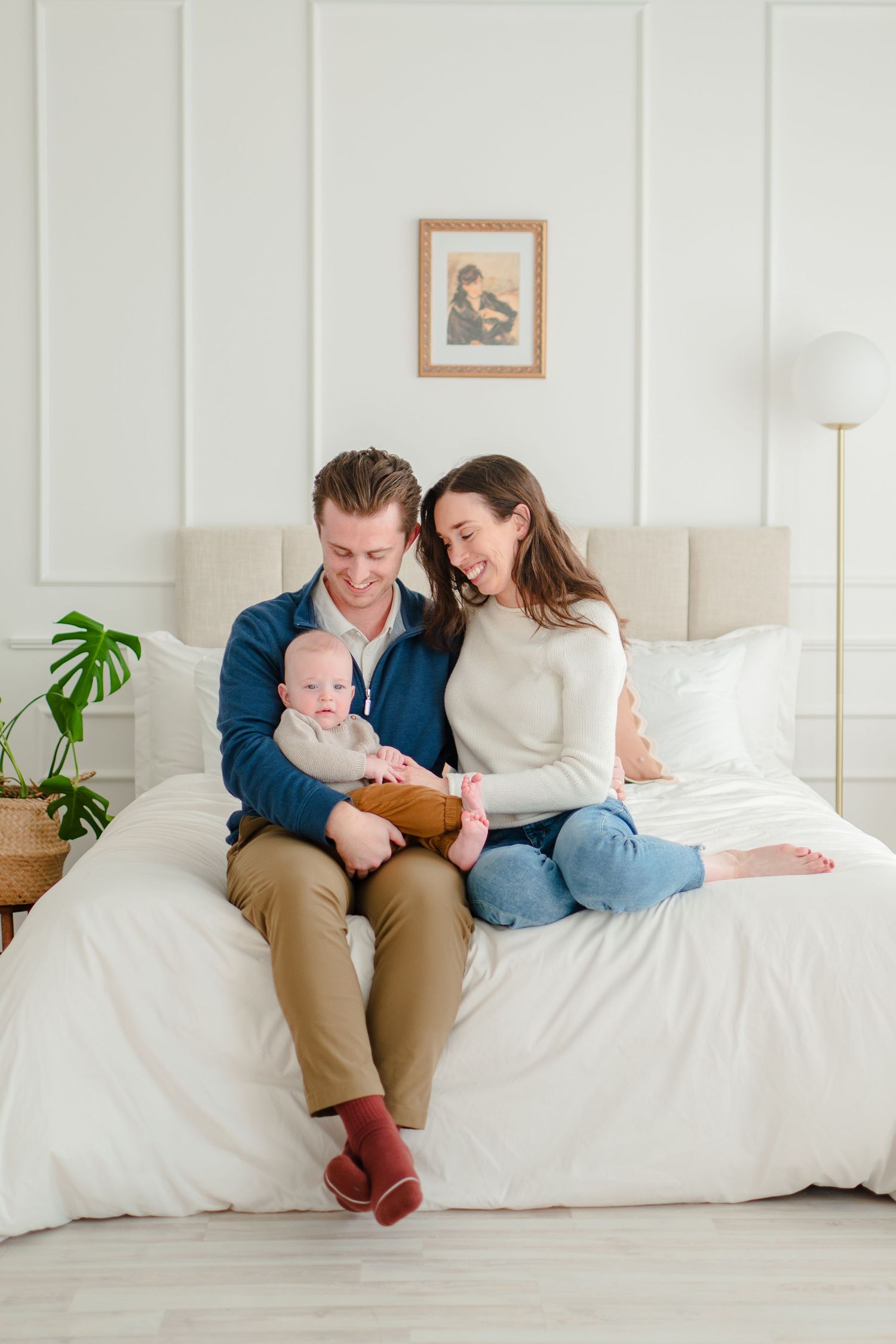 Family spending quality time together reading a book on a white bed with minimalist decor in a bright room.
