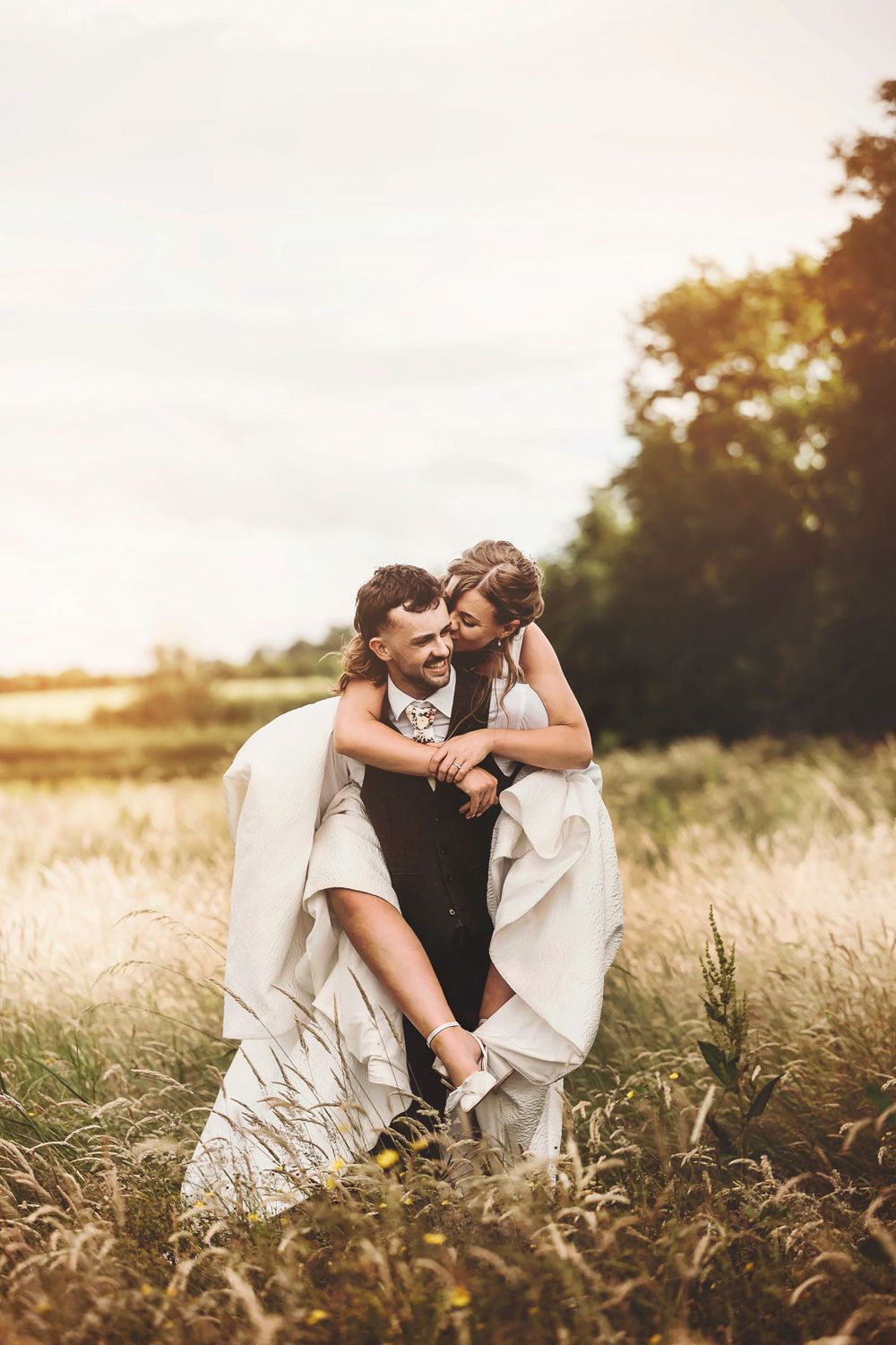 Romantic couple shares intimate moments together in a golden sunlit field of tall grass at sunset.