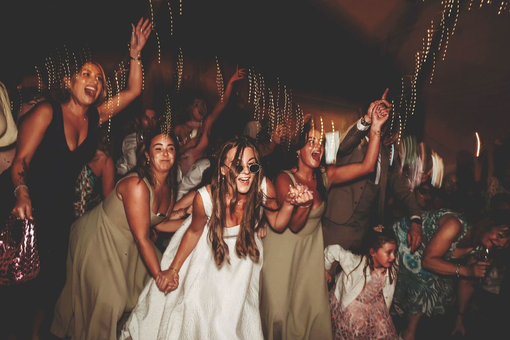 Wedding reception guests dancing and celebrating on a dimly lit dance floor.