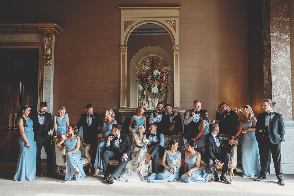 Wedding party poses outdoors in coordinated black and light blue attire in front of wooden structure.