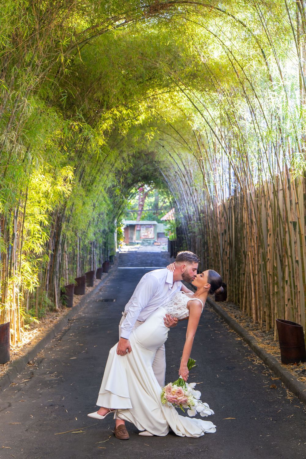 A romantic wedding moment in a bamboo-lined pathway with lush green foliage creating a natural tunnel canopy at Conrad Bali Resort.
