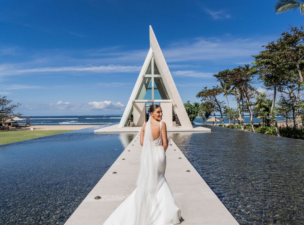 Bride in flowing white dress poses on walkway surrounded by water at luxury tropical beach resort location.