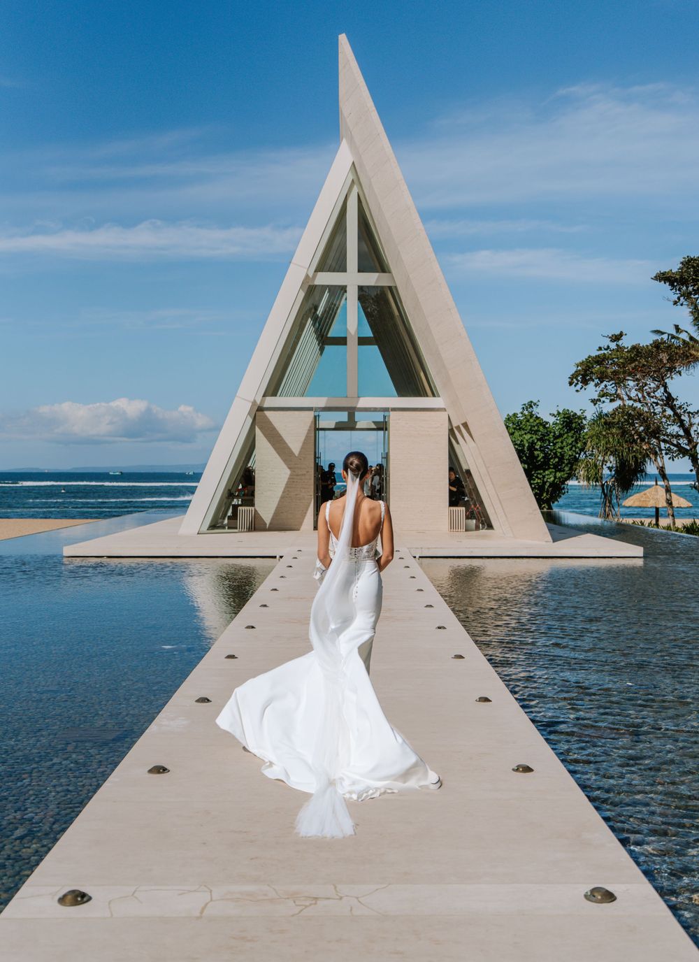 Stunning oceanfront wedding chapel with A-frame architecture captures dramatic angles against blue sky and sea at Conrad Bali Resort.