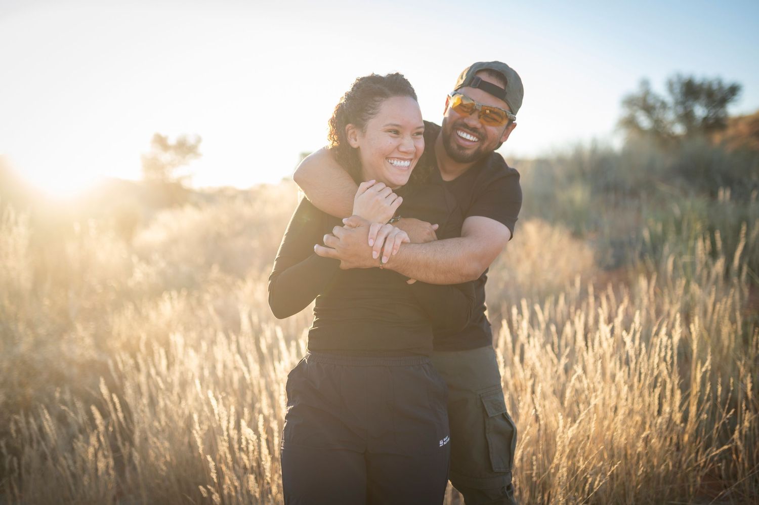 A couple embraces in a golden wheat field during sunset creating a romantic silhouette against warm sunlight.