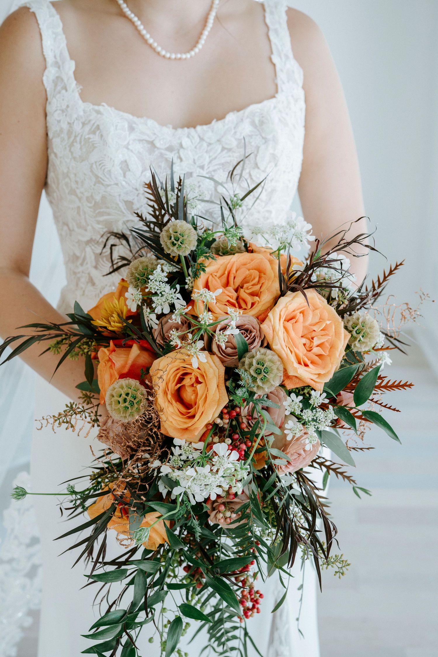 Romantic peach garden roses and succulents bridal bouquet with natural greenery and wildflowers against white background.