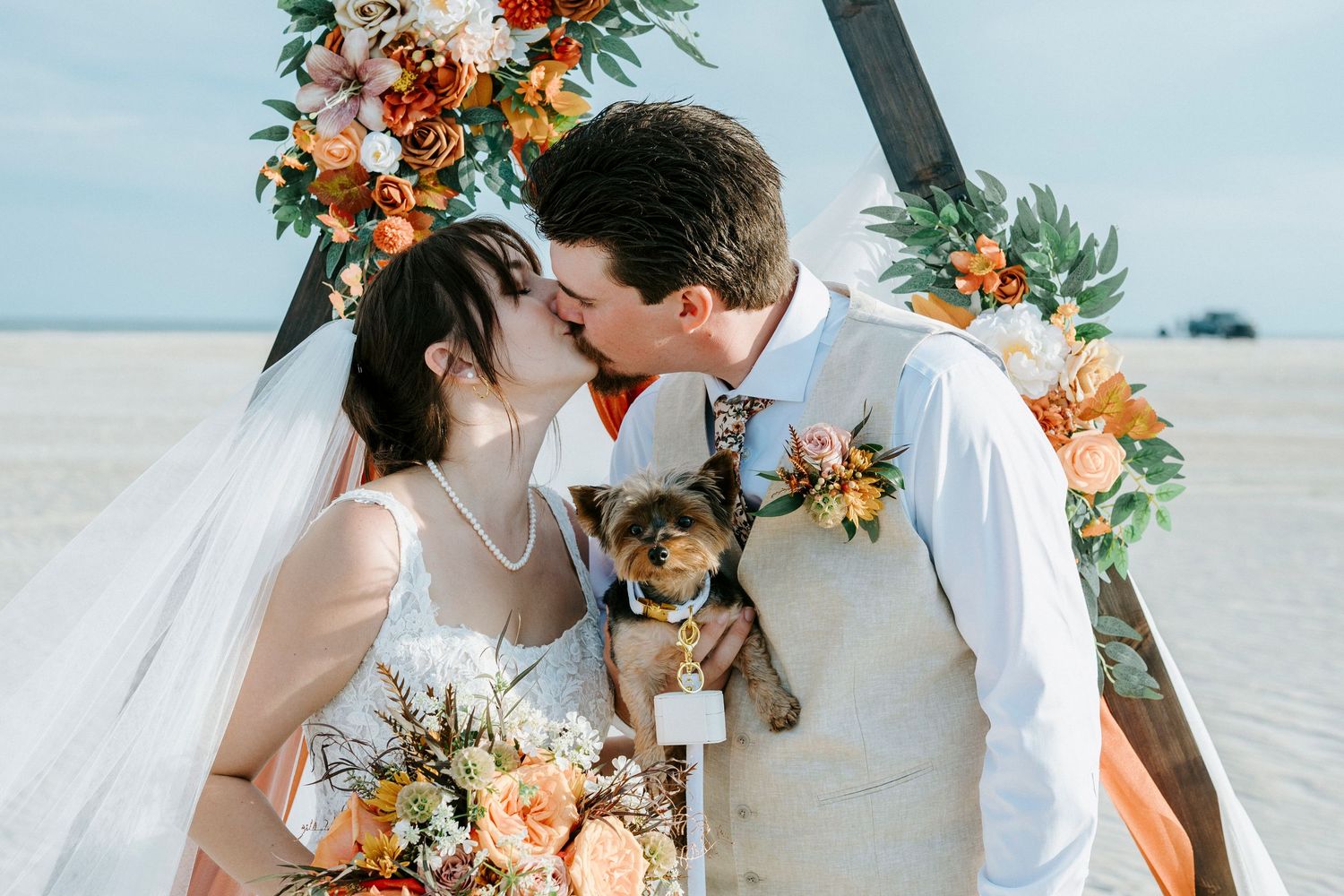 A romantic beach wedding with colorful tropical flowers, white attire, and a sweet pup involved in the ceremony.