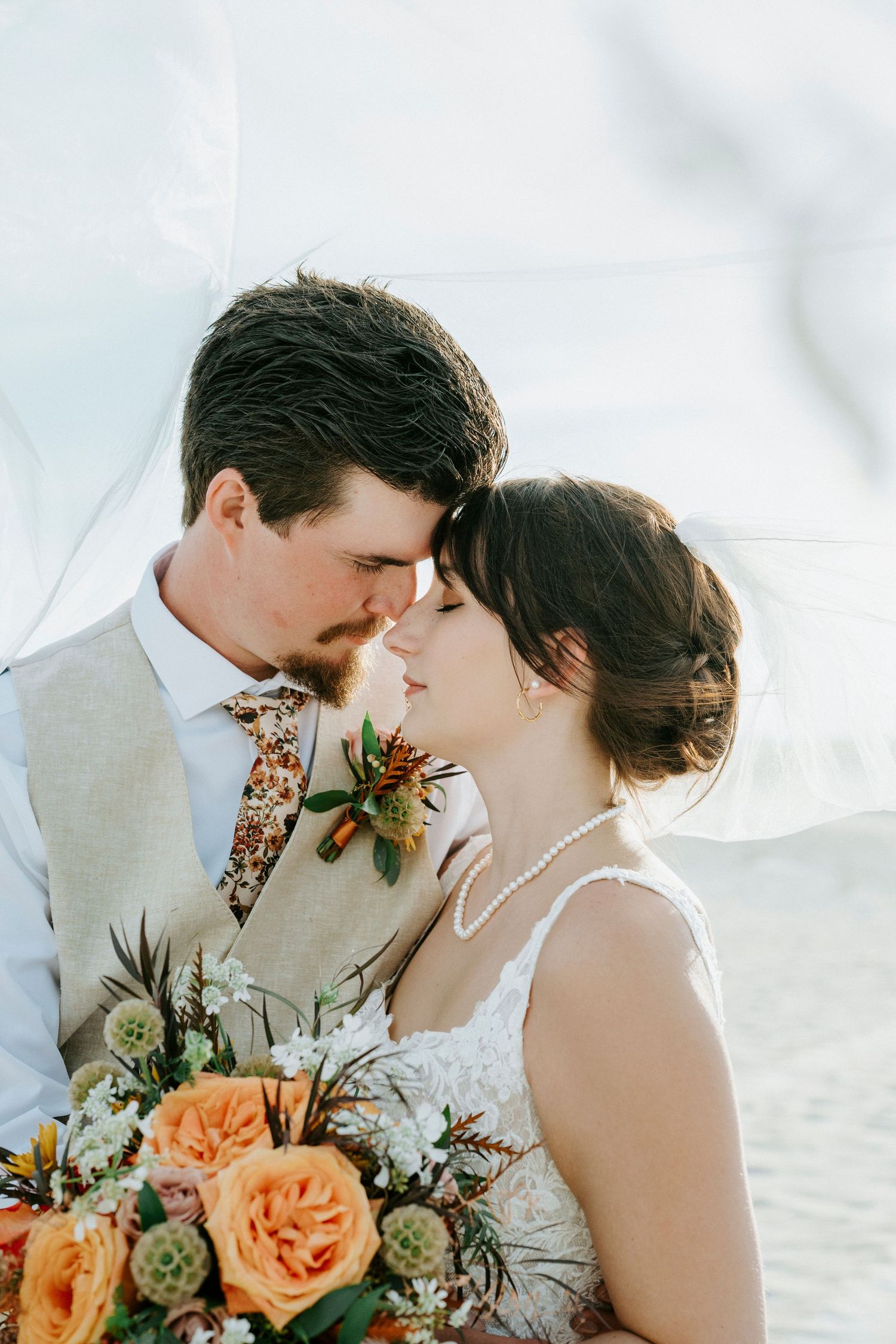 Intimate wedding couple pose with peach floral bouquet and succulent details against a light background.