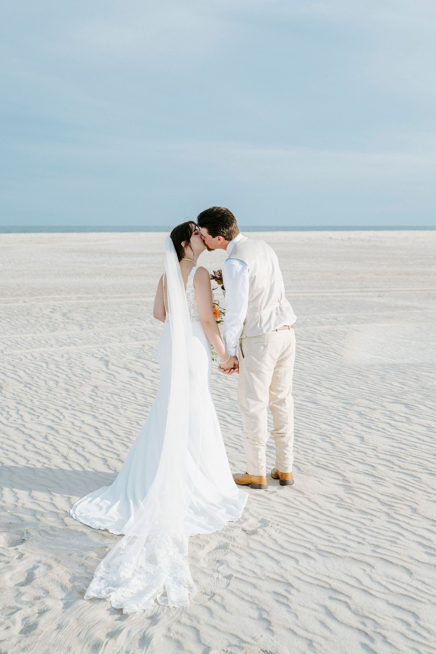 Romantic wedding portraits on pristine white sand beach with flowing bridal gown and light-colored attire.