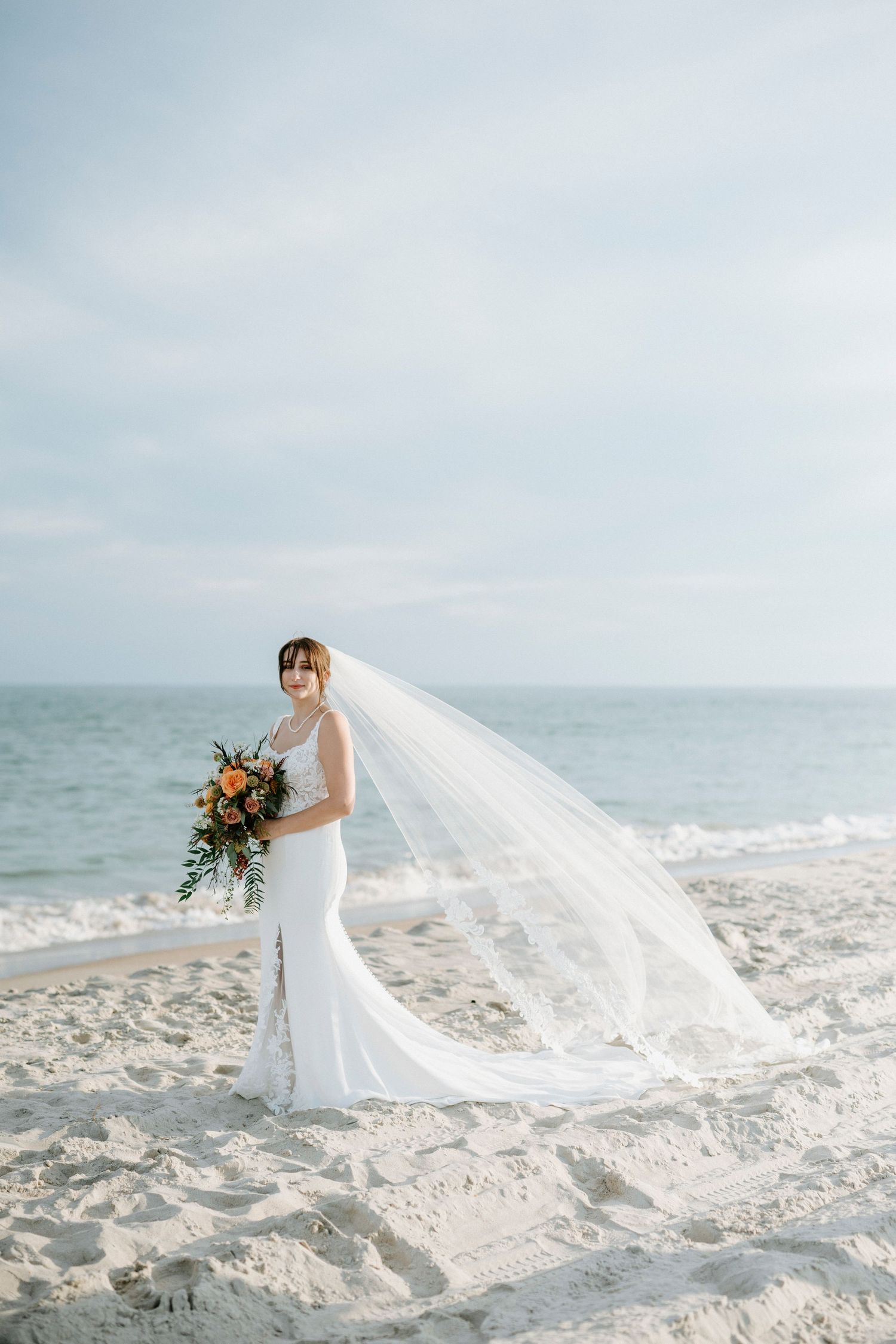 Beautiful beach wedding scene with flowing white dress and veil catching the ocean breeze at sunset.