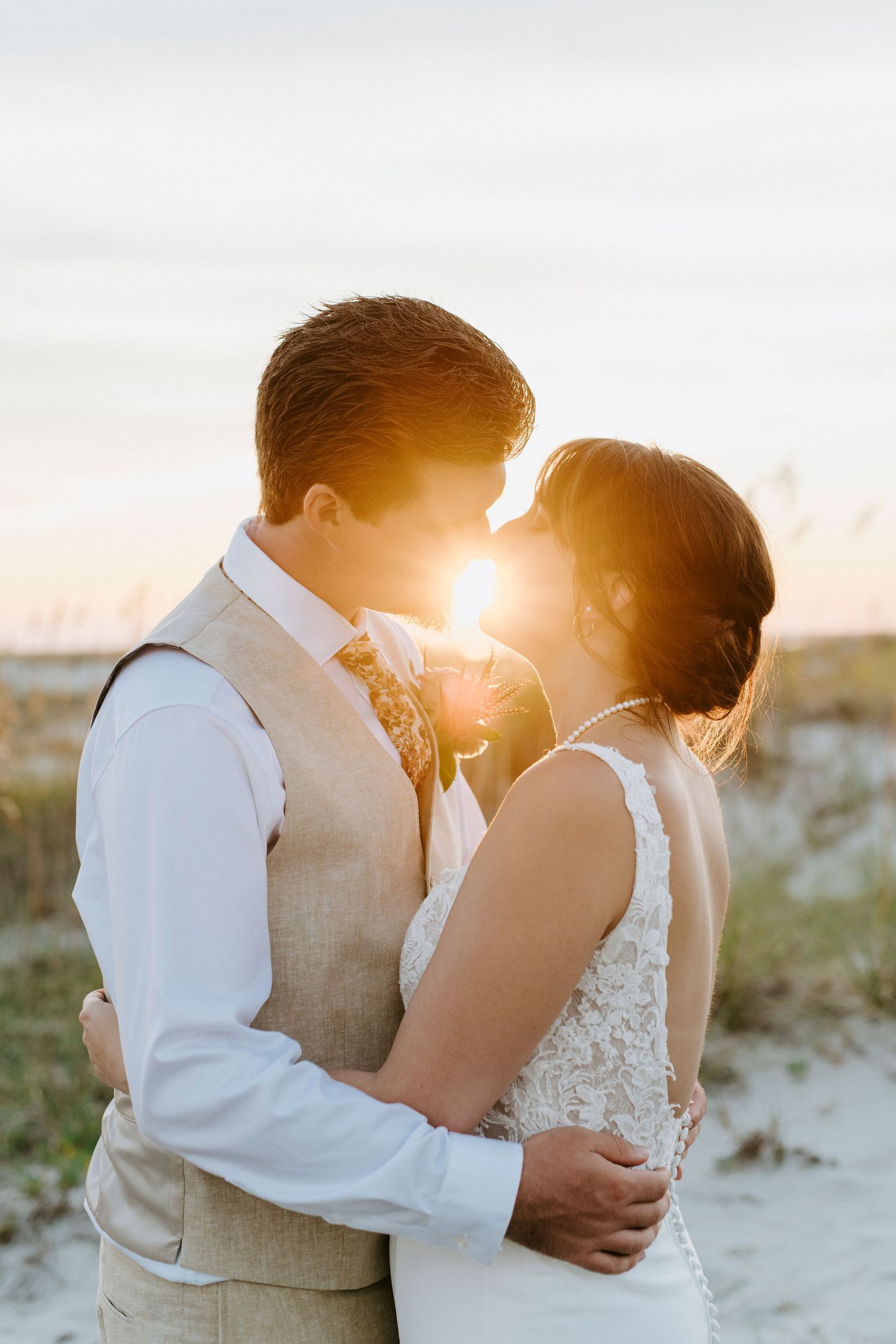 A romantic sunset beach wedding photo silhouetted against golden sunlight in a warm coastal setting.