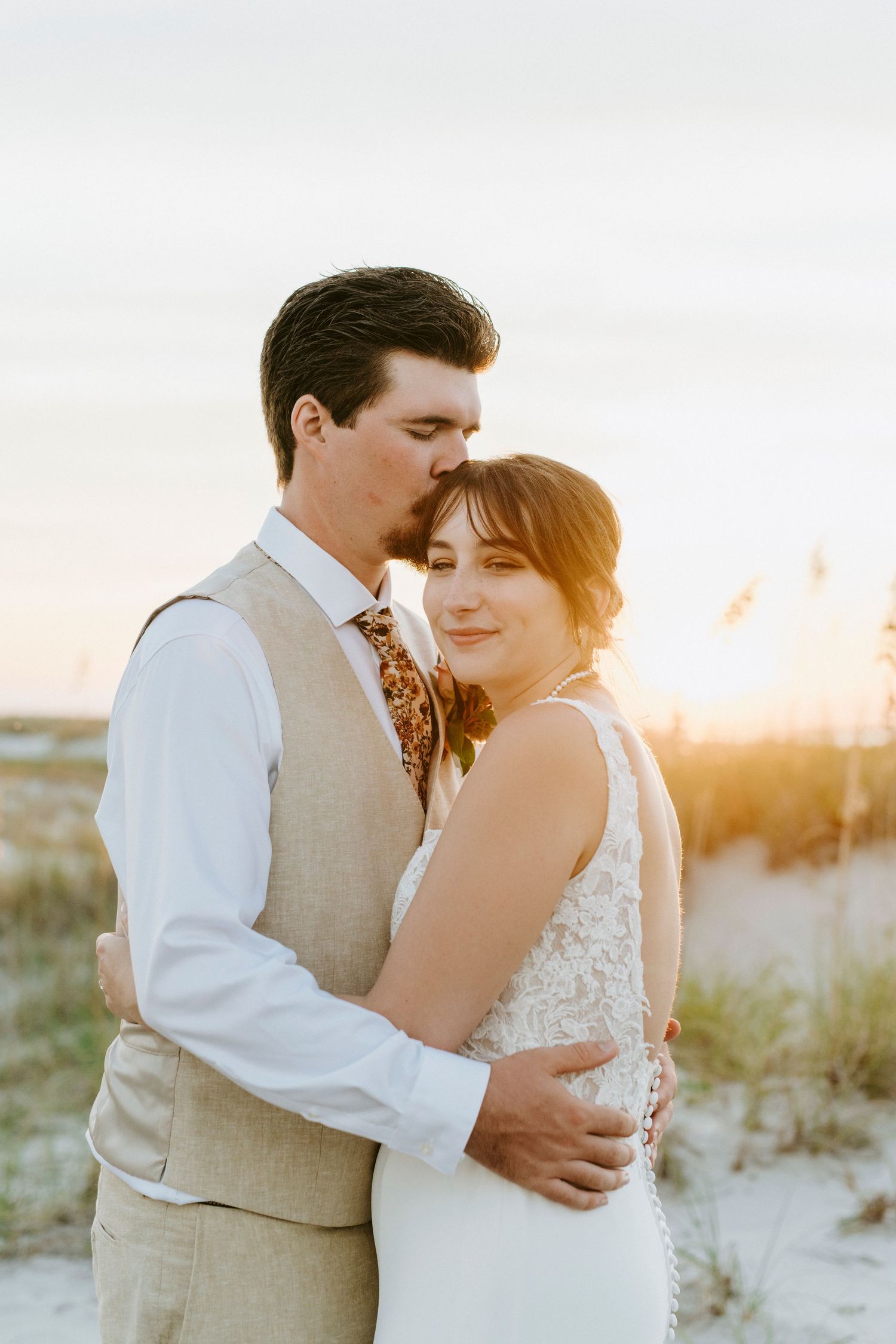 Newlyweds share intimate moments at sunset on a sandy beach as golden light illuminates their romantic poses.