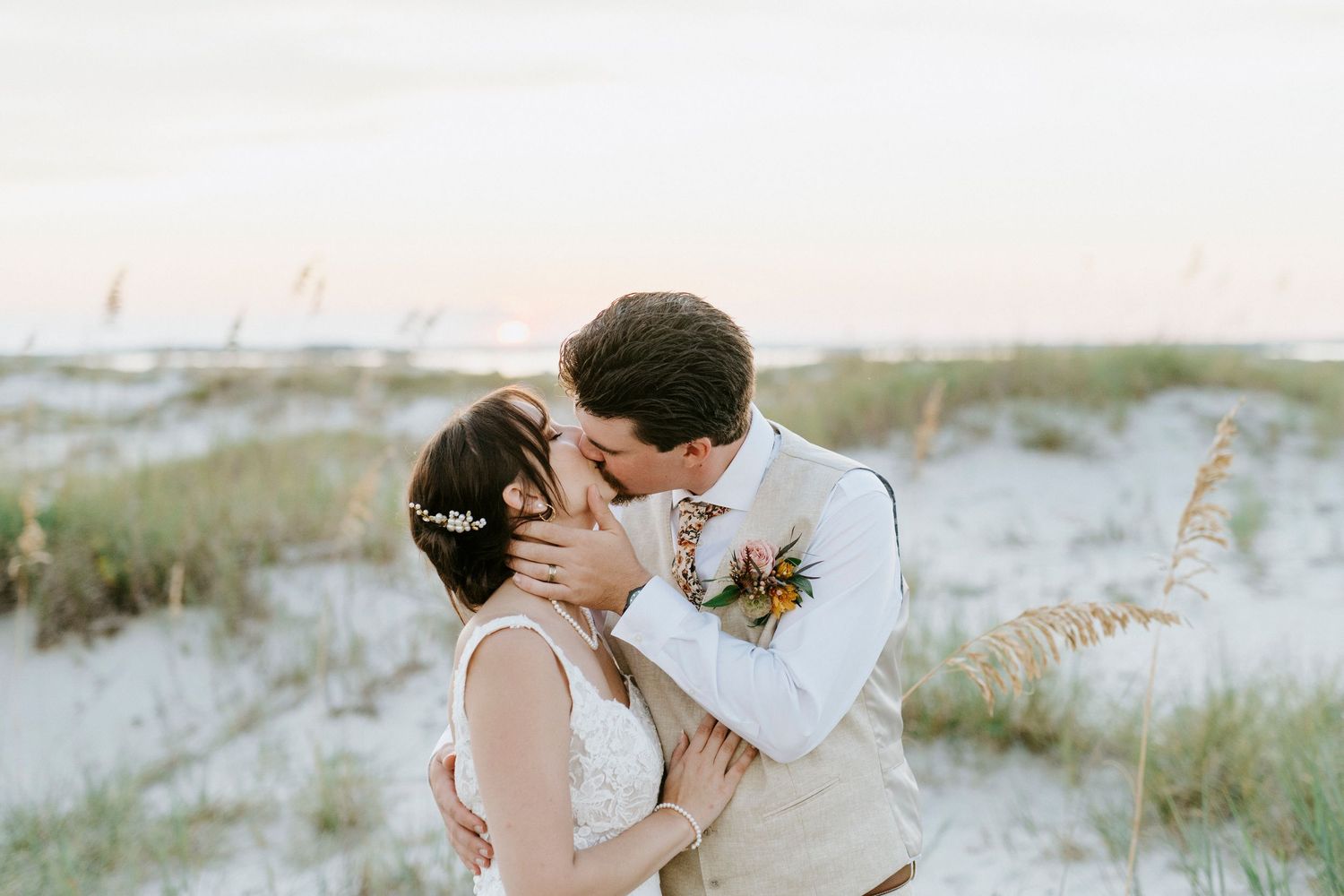 Modern wedding couple sharing intimate moment on beach with floral details and sea breeze.