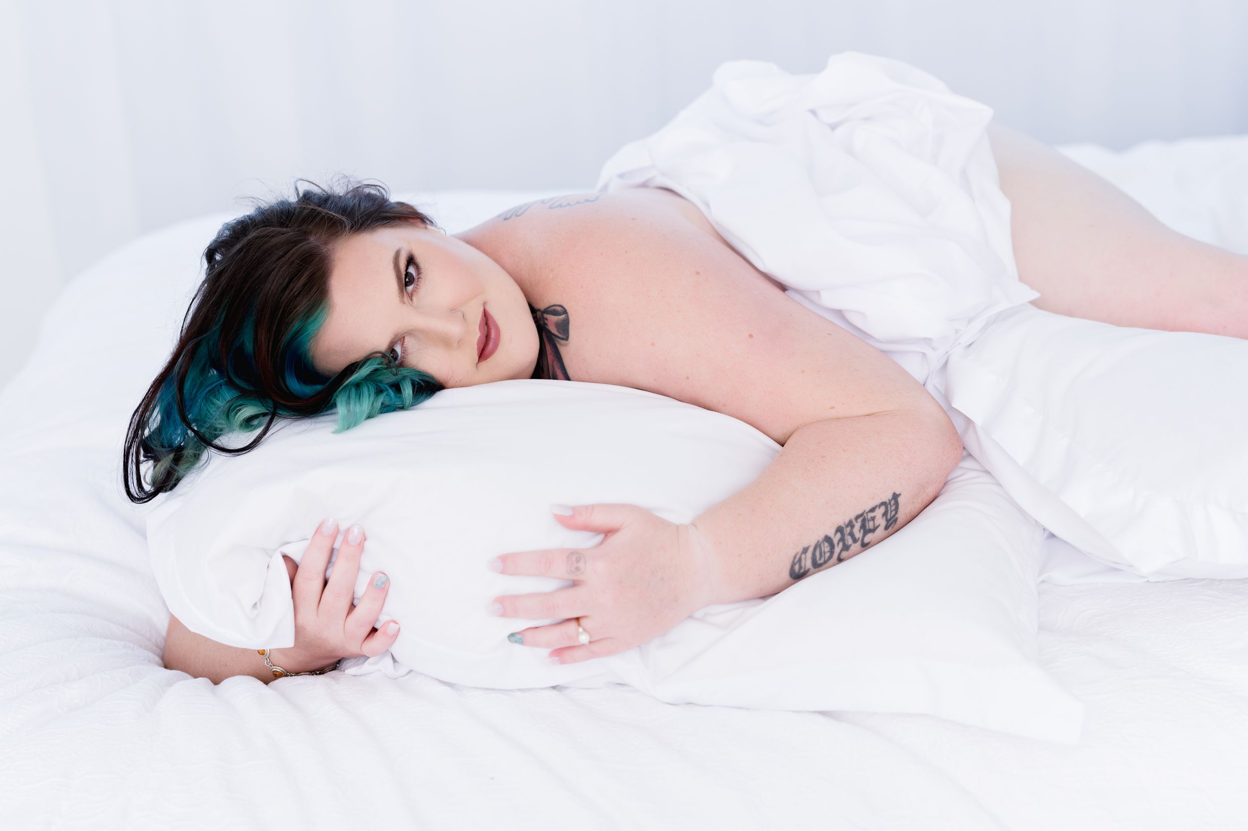 Person in white bedding poses with teal hair highlights on white bed.