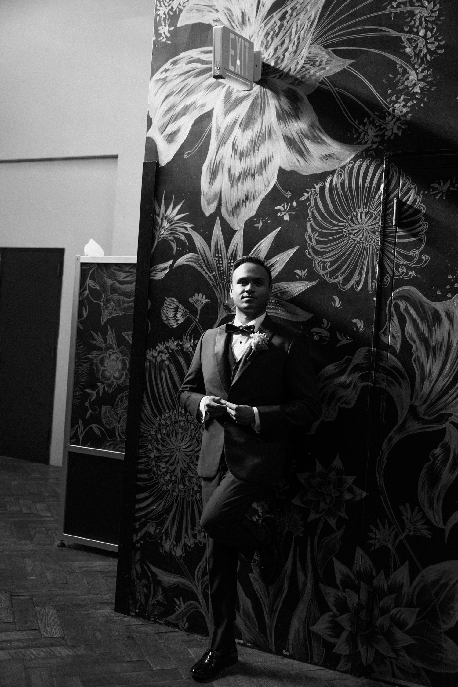 Artistic black and white portrait against a floral wallpaper backdrop.