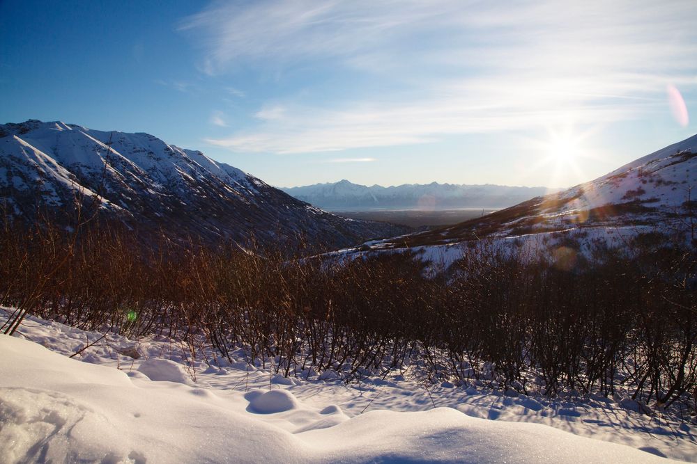 A panoramic view of snow-covered mountain ranges during winter with sunlight casting shadows across the terrain.