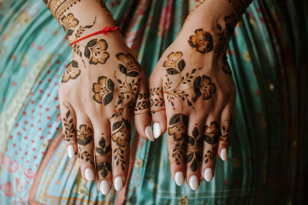 Intricate henna designs featuring floral patterns adorn hands resting on a turquoise fabric.