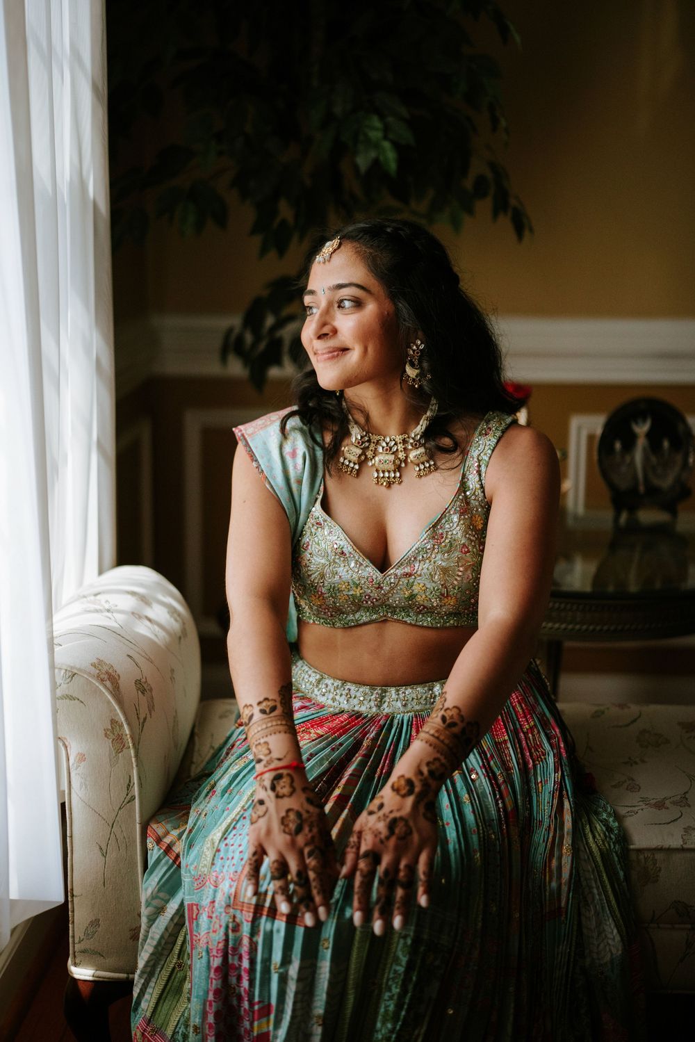 Traditional Indian bridal portraits showing intricate henna designs and elegant wedding attire by a window.