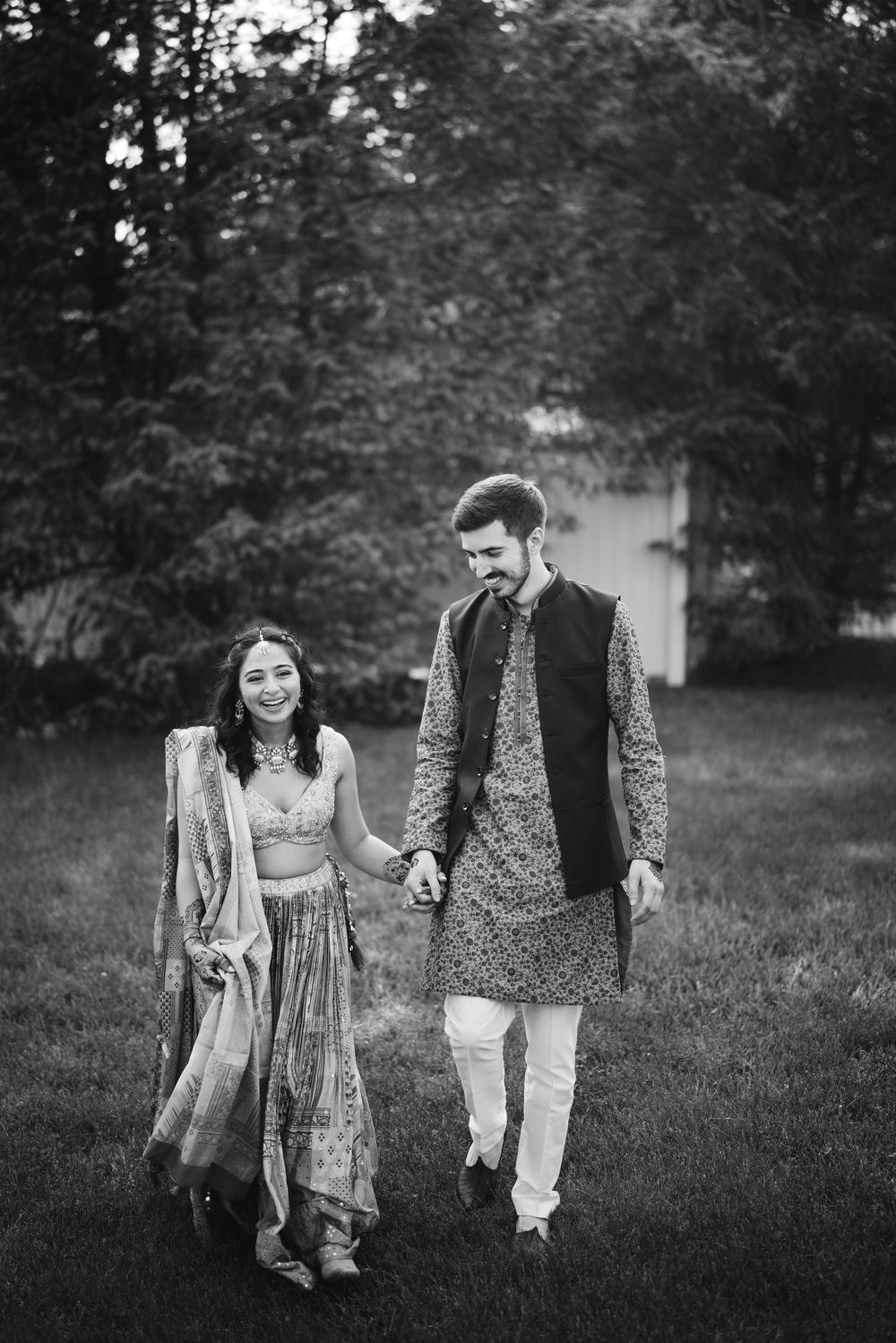 Black and white romantic photoshoot of a couple walking together in a garden setting wearing traditional Indian attire.