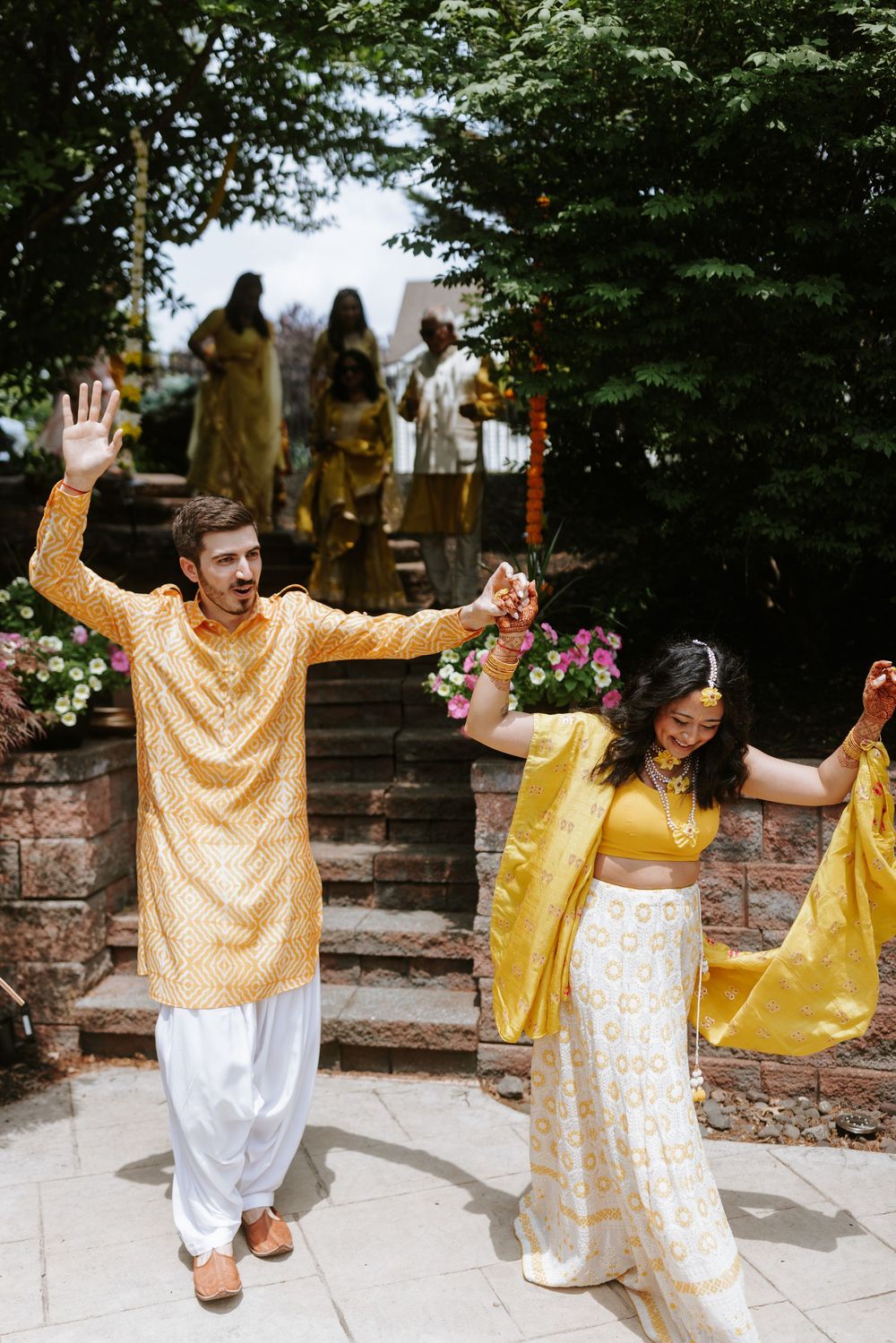 Wedding guests dancing and celebrating in yellow and white traditional Indian attire by a poolside.