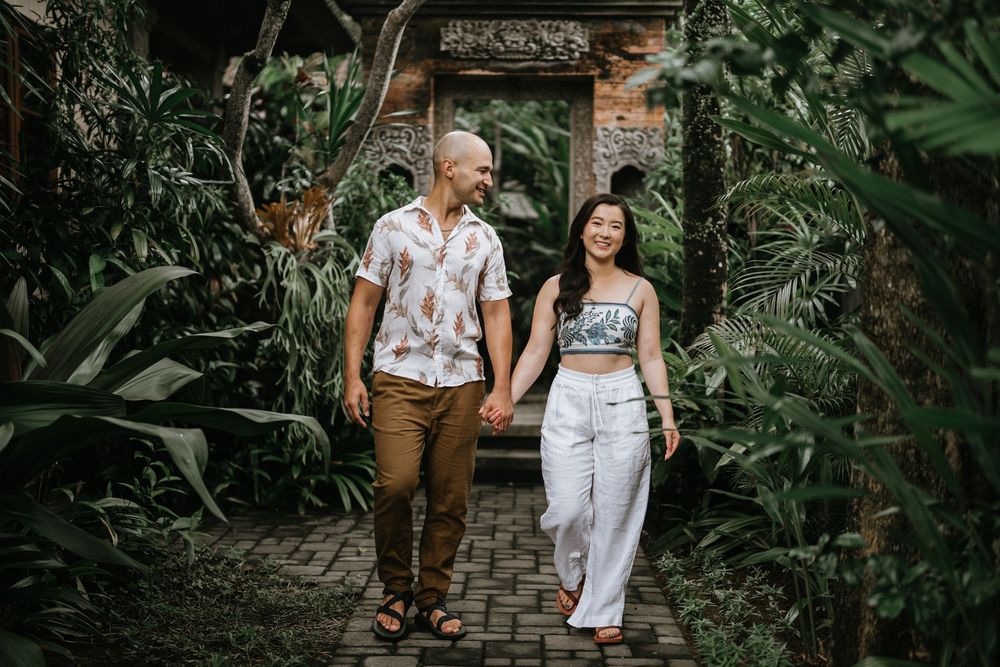 Couple walking through traditional Balinese garden gateway surrounded by tropical plants.