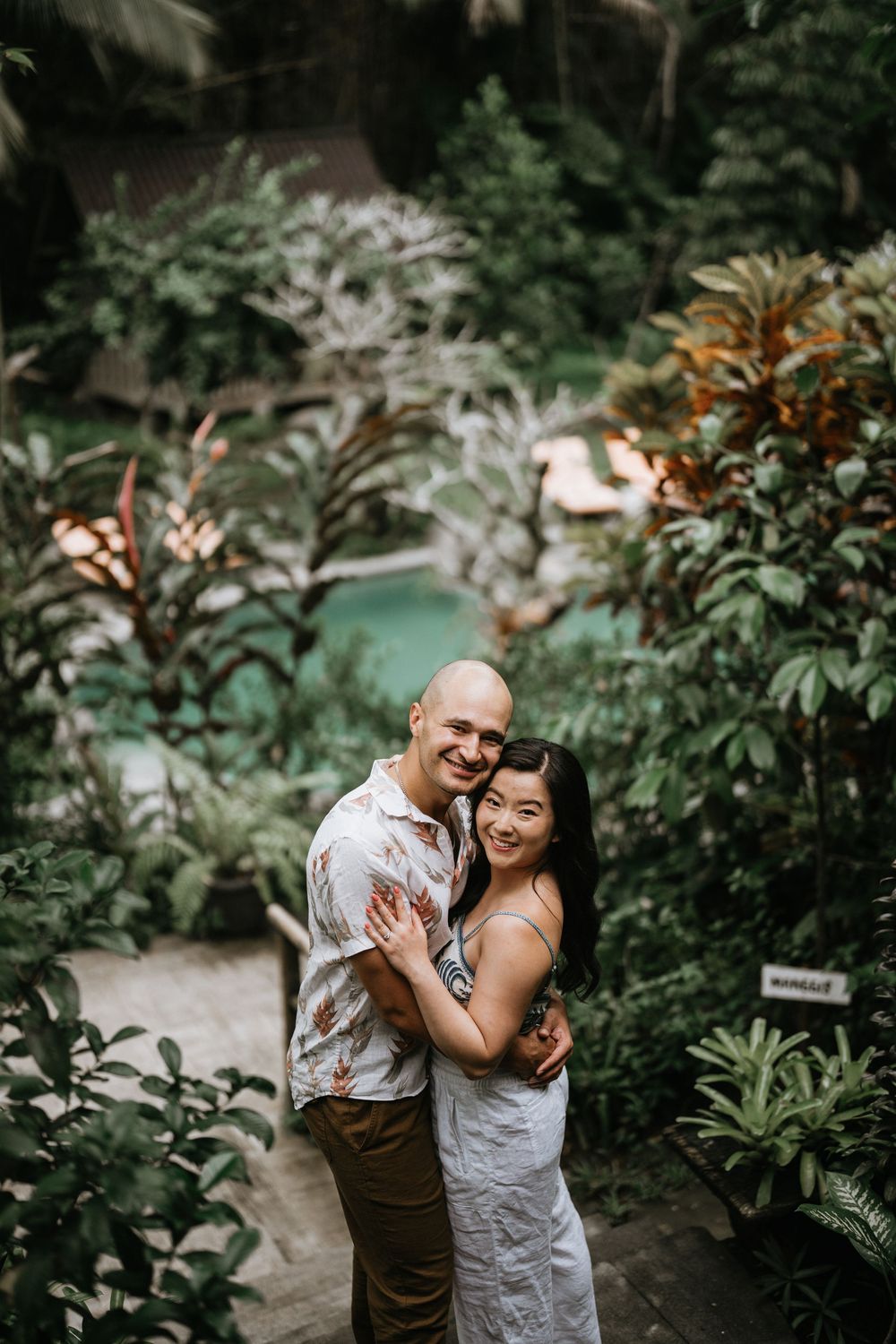 Couple embracing and laughing in tropical garden with pool in background.