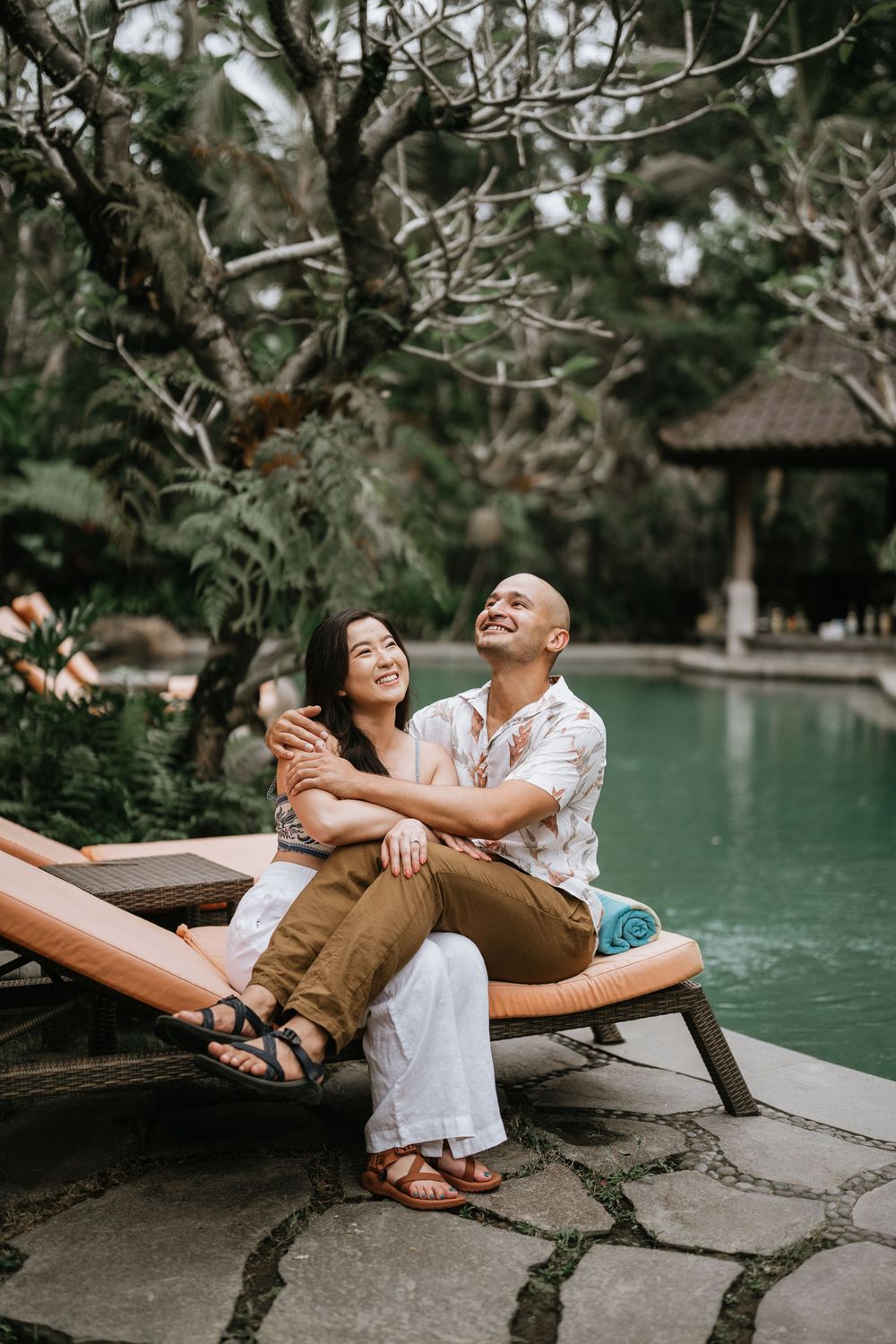 Happy couple sharing intimate moment on pool deck surrounded by tropical trees.