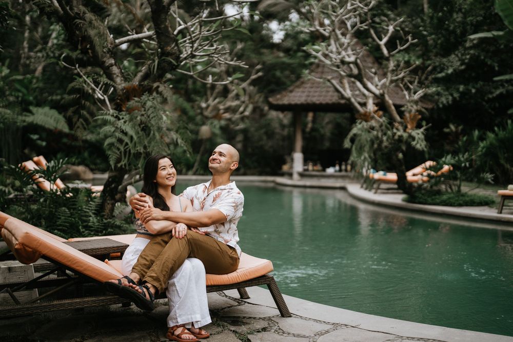Couple relaxing on lounger by tropical pool surrounded by lush gardens.