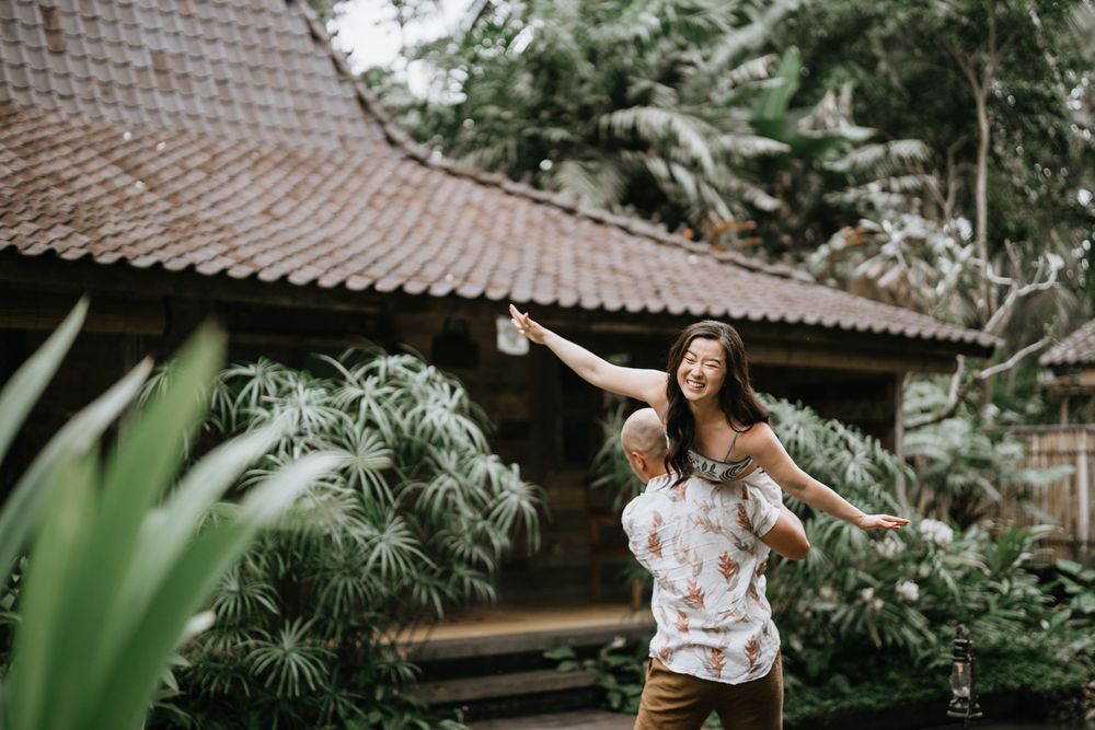 A couple poses playfully in a lush tropical garden setting with bamboo structures and palm trees.