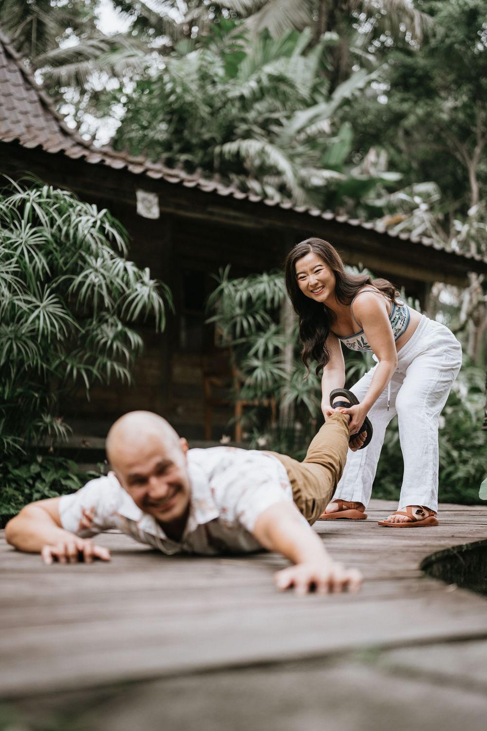 Two people lying on wooden deck surrounded by tropical greenery creating fun photo poses.