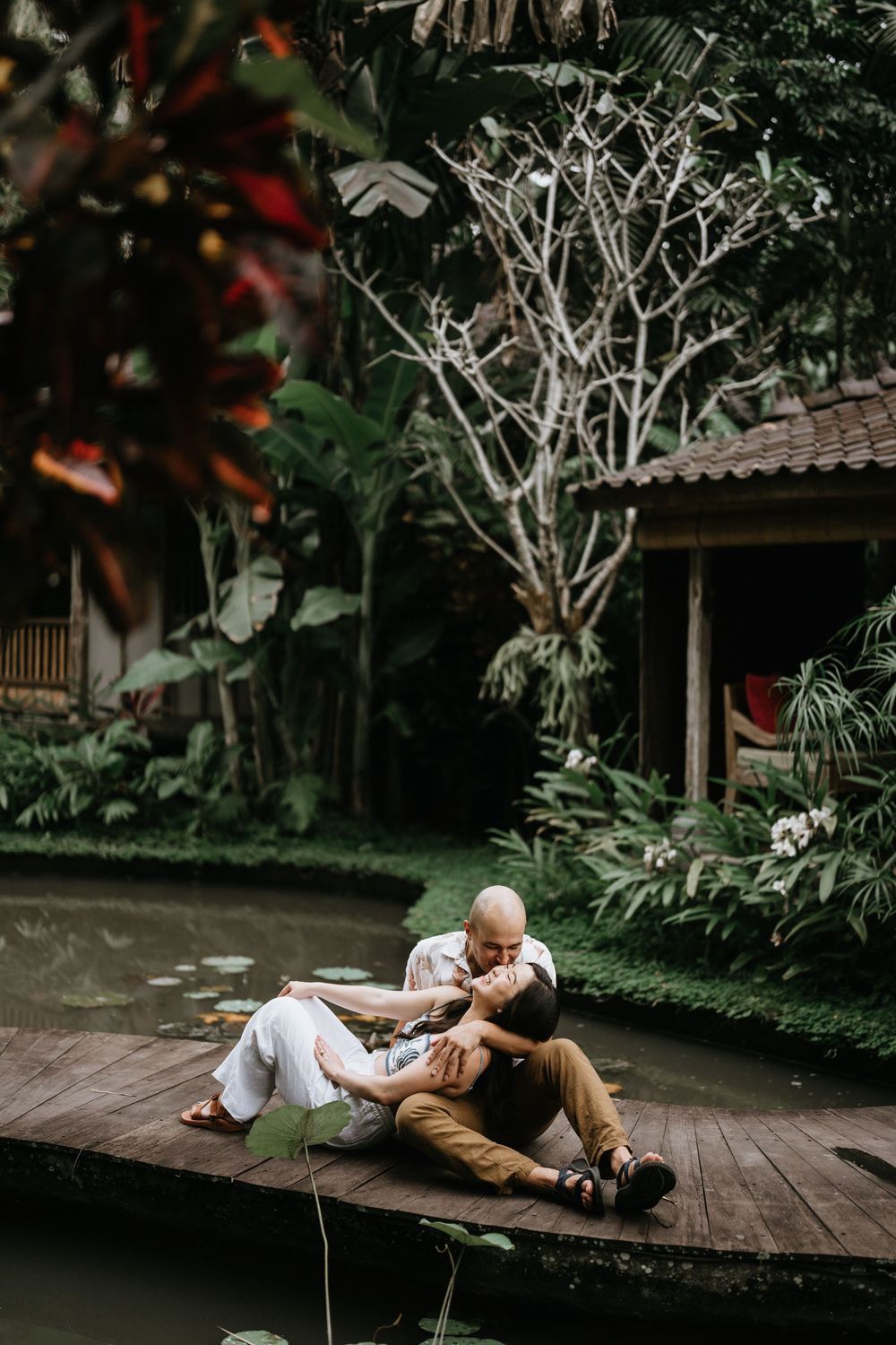 Romantic couple poses on wooden deck surrounded by lush tropical vegetation.