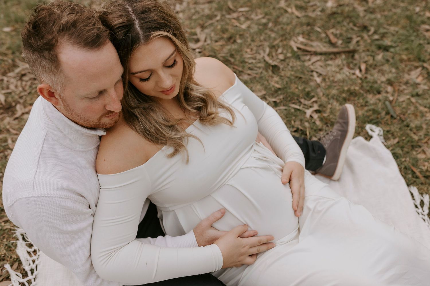 Intimate maternity photo of couple in white outfits embracing outdoors.