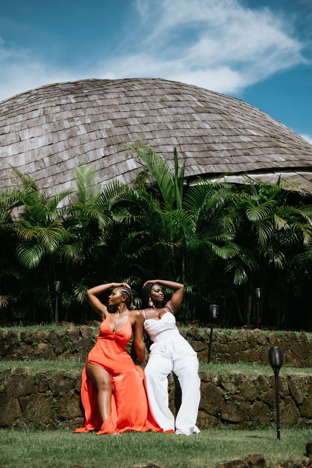 Two friends strike dramatic poses in formal dresses against domed building surrounded by palm trees.