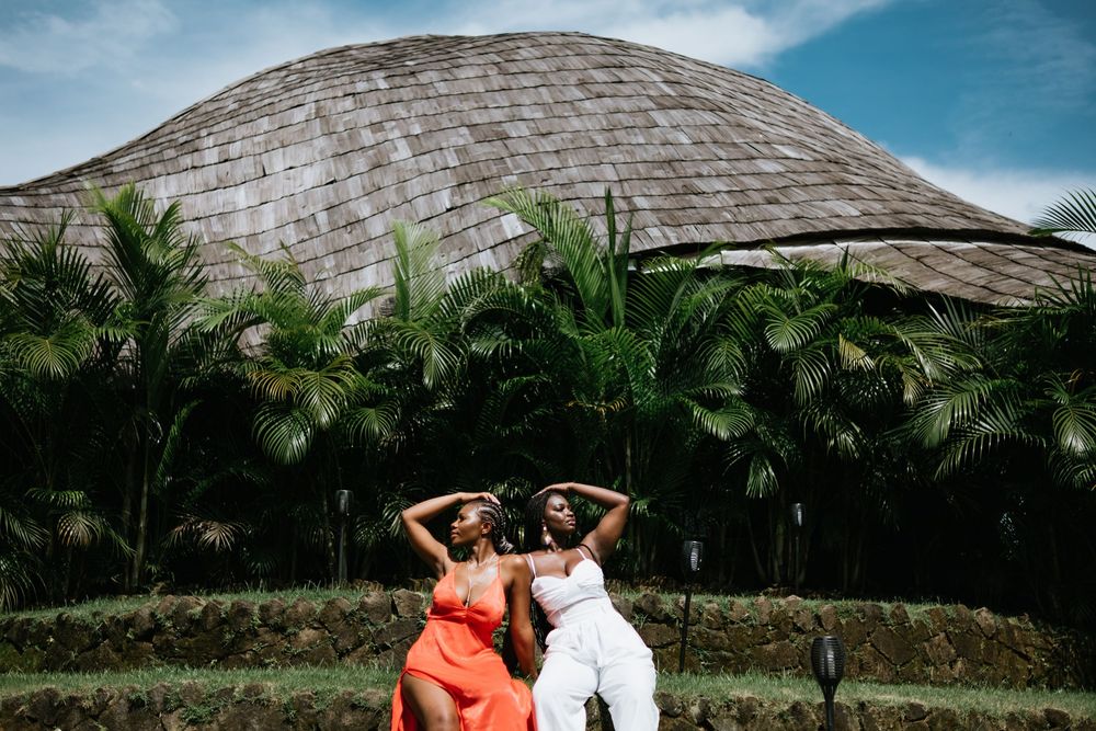 Two women in contrasting outfits pose playfully against dome structure and tropical landscape.