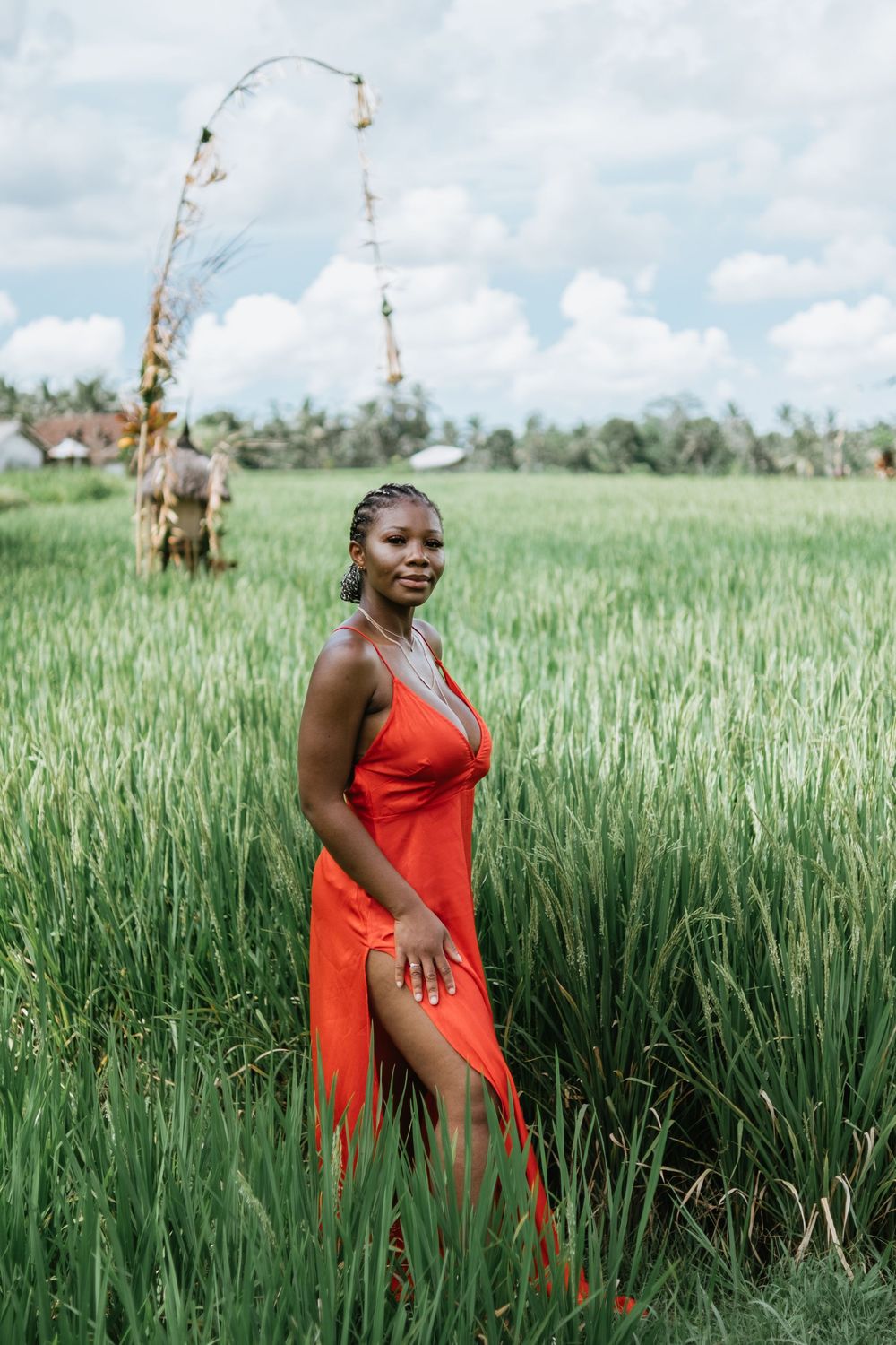 A figure in a vibrant red dress poses gracefully in a lush green field under a bright blue sky.
