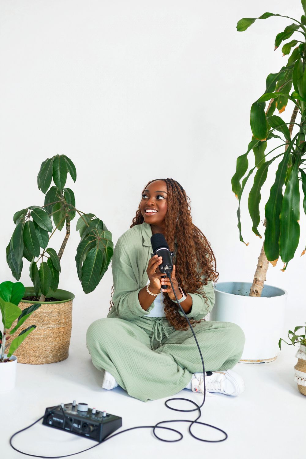 Person recording audio content surrounded by large leafy plants in bright studio setting.