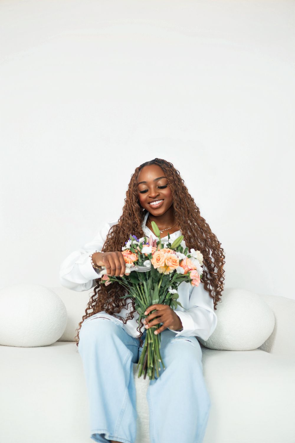 Person in casual attire arranging peach-colored flowers on white couch.