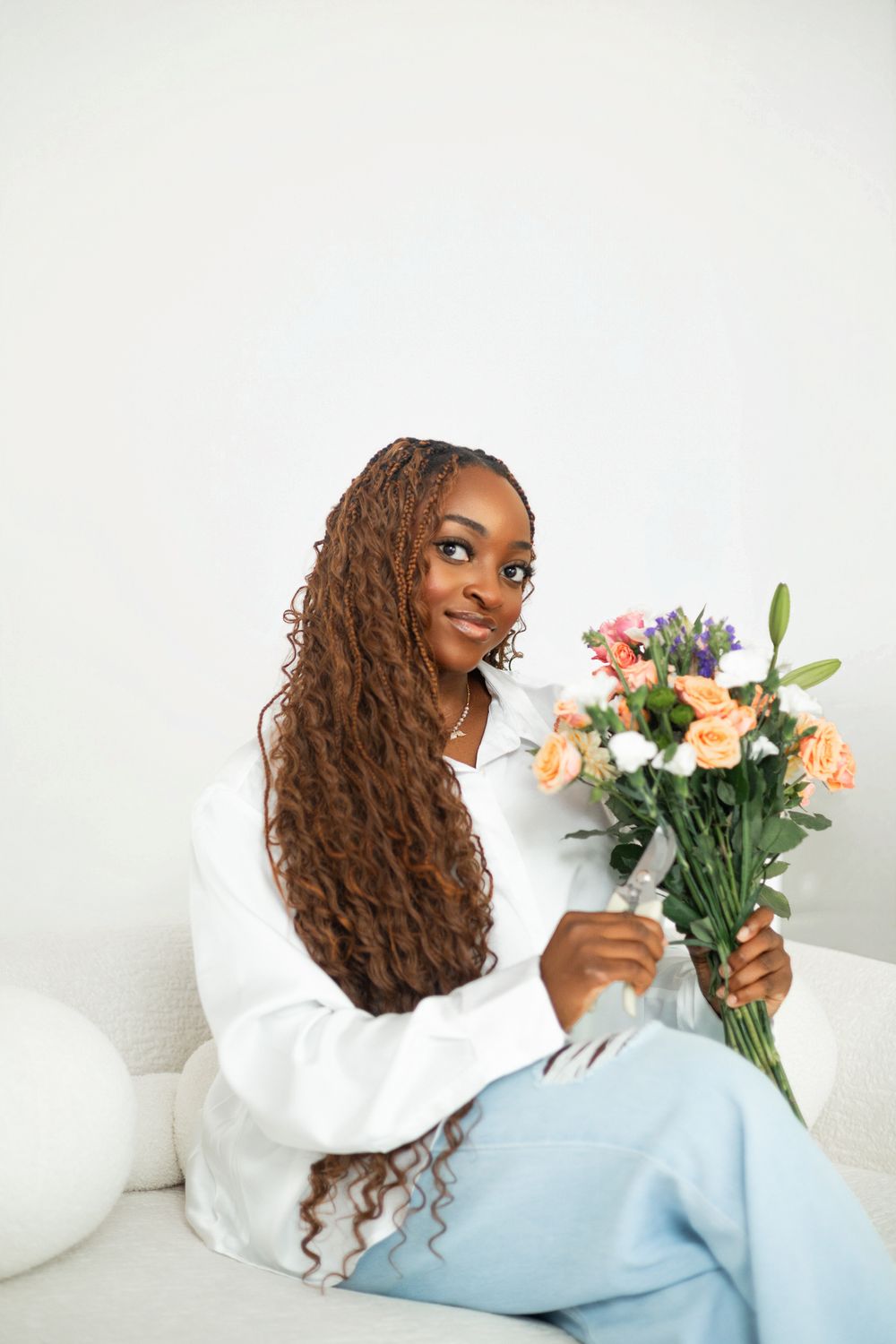 A person in a white sweater holds a bouquet of fresh flowers while lounging on a light blue couch.