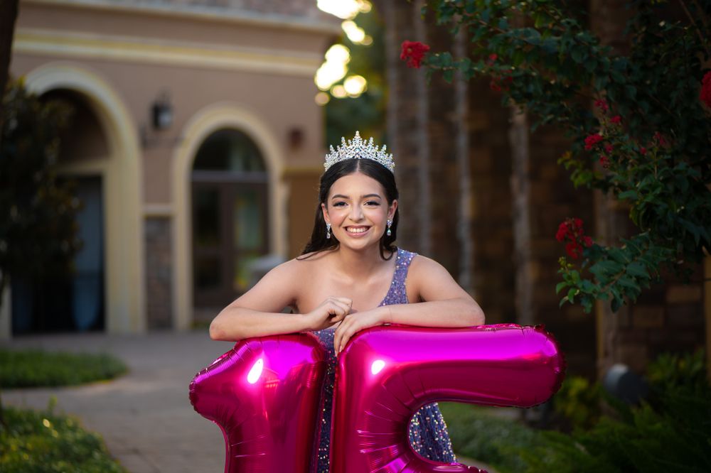Festive quinceañera pose with large pink number 15 balloons and crystal crown.