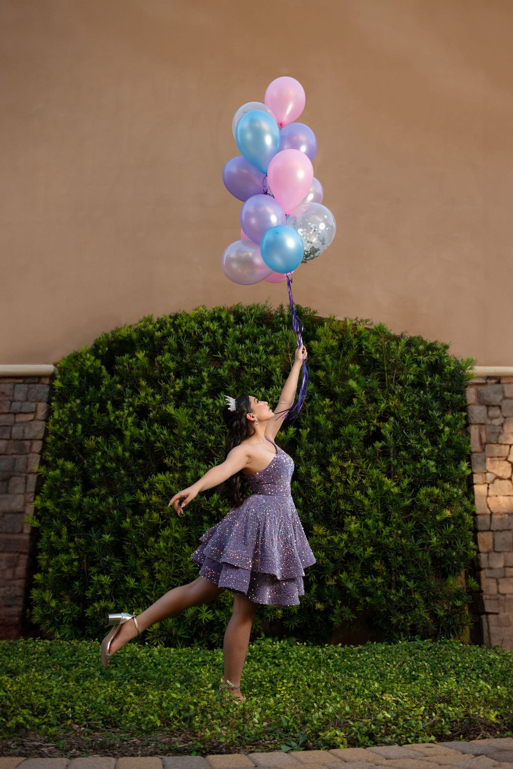 Whimsical dance pose with pastel balloons while wearing a purple sparkly dress.