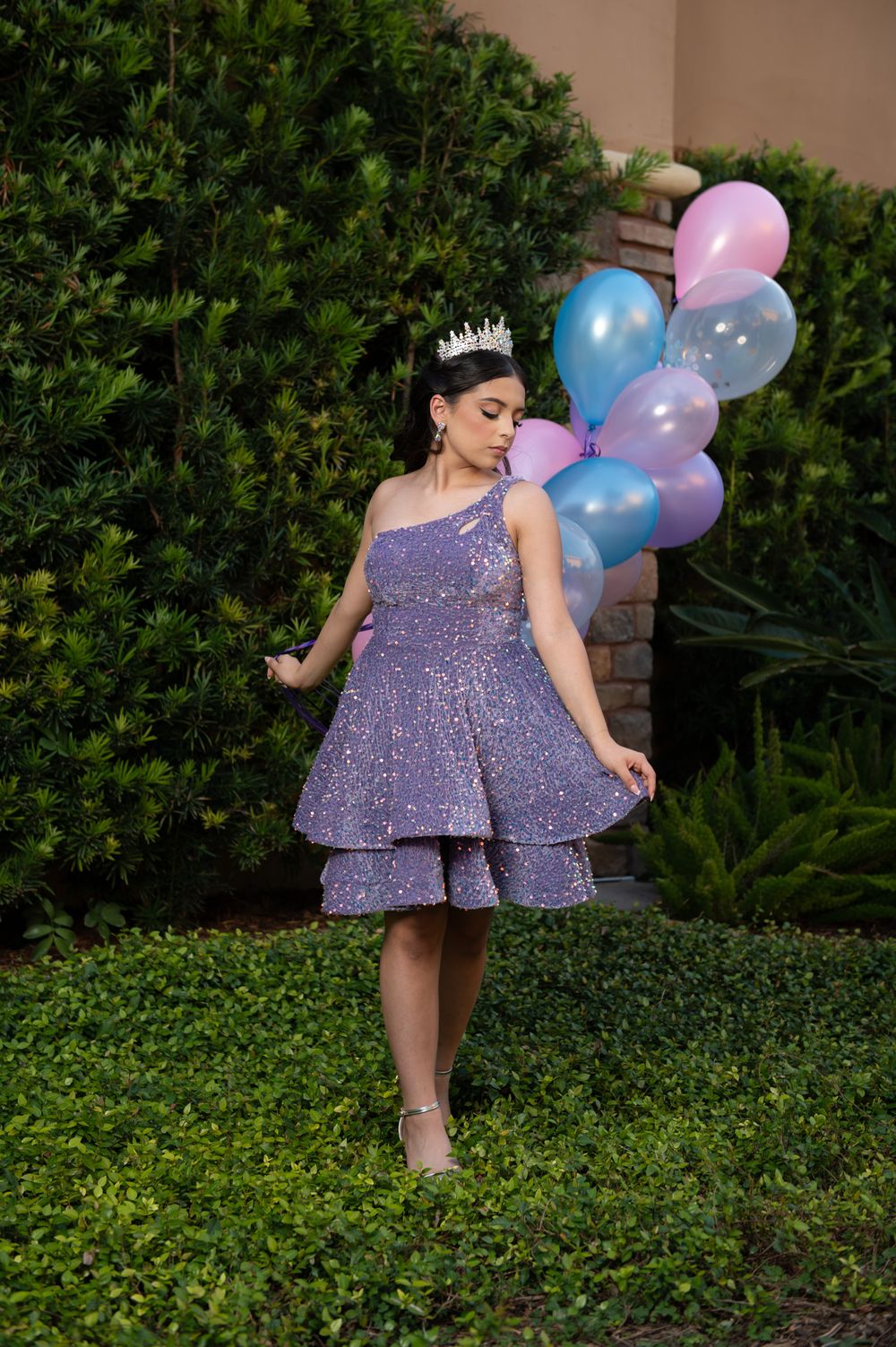 A sparkling purple party dress with tiered skirt is complemented by pastel balloons in an outdoor garden setting.