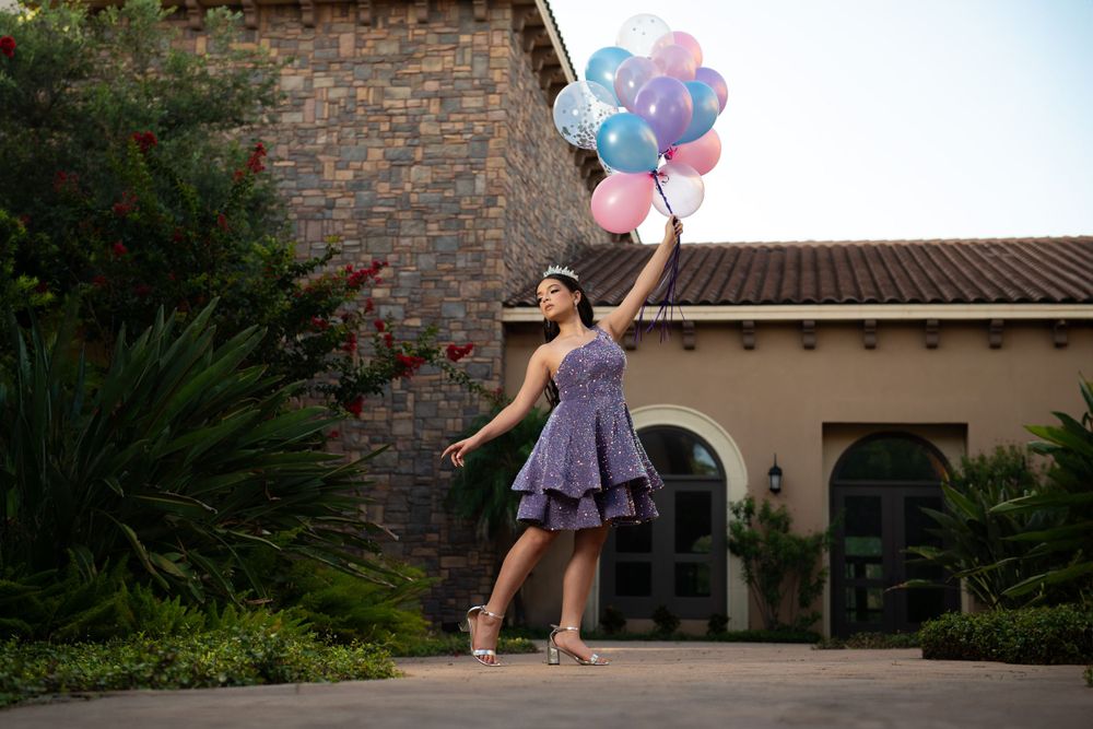 Joyful celebration pose with balloons against Mediterranean-style architecture.
